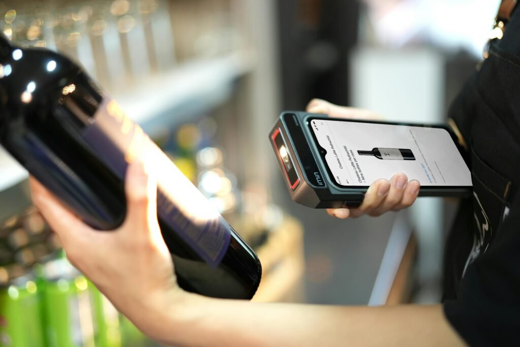Close-up of a person scanning a wine bottle with a portable scanner in a store.